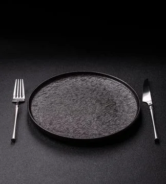 An empty round ceramic plate, knife, and fork as a dining table setting. An.. Stock Photos