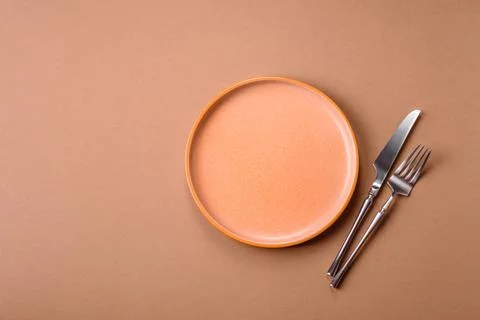 An empty round ceramic plate, knife, and fork as a dining table setting. An.. Stock Photos