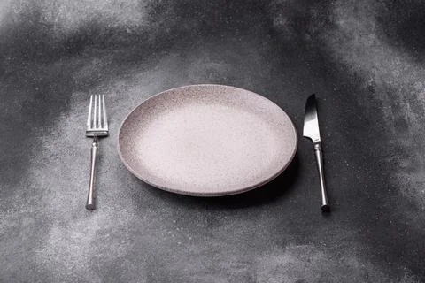 An empty round ceramic plate, knife, and fork as a dining table setting. An.. Stock Photos