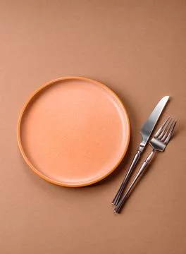 An empty round ceramic plate, knife, and fork as a dining table setting. An.. Stock Photos