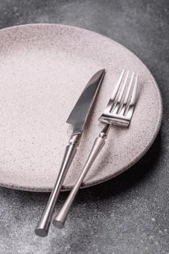 An empty round ceramic plate, knife, and fork as a dining table setting. An.. Stock Photos