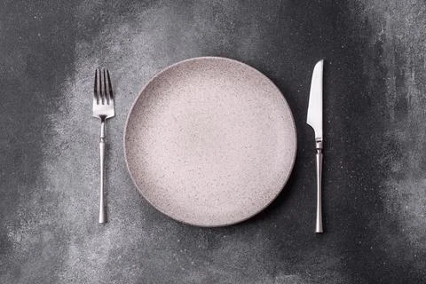 An empty round ceramic plate, knife, and fork as a dining table setting. An.. Foto stock