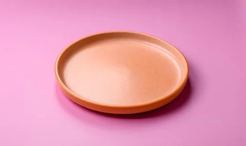 An empty round ceramic plate on a pink background as a kitchen utensil. An .. Stock Photos