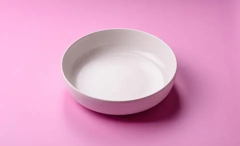 An empty round ceramic plate on a pink background as a kitchen utensil. An .. Stock Photos