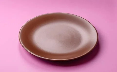 An empty round ceramic plate on a pink background as a kitchen utensil. An .. Stock Photos