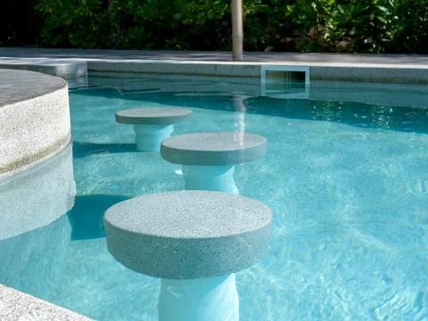 Empty round terrazzo bar stools seat in clean and clear water swimming pool.. Foto stock