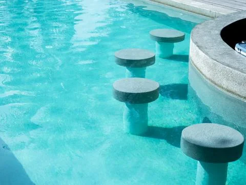 Empty round terrazzo bar stools seat in clean and clear water swimming pool.. Stock Photos