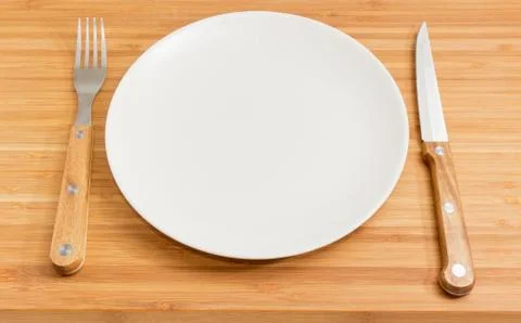 Empty round white plate, fork and knife with wooden handles Stock Photos