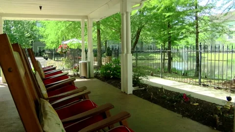 Empty Row Of Rocking Chairs Face Pond At Retirement Community Video stock 133733247