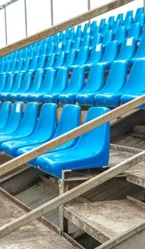 Empty rows of blue and pink plastic stadium seats behind a safety net. Stock Photos