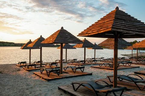 Empty rows resting places on evening sandy beach with brown wooden loungers Stock Photos