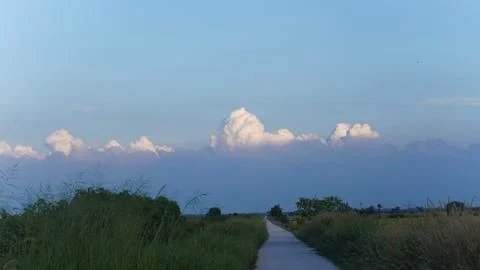 Empty rural path through green fields under dramatic evening sky with clouds Stock Photos