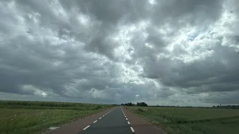 Empty rural road stretching through flat green fields beneath dramatic storm Stock Photos