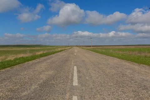 Empty Rural Road Through Green Fields Under a Blue Cloudy Sky Foto stock