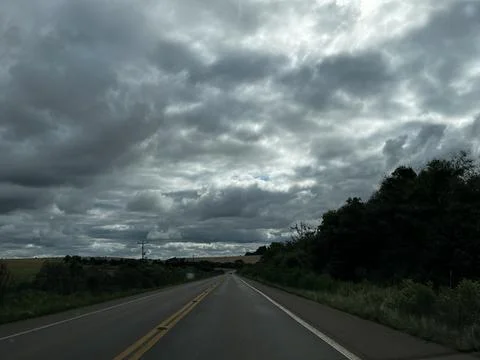 Empty rural road under dramatic cloudy sky, leading towards the horizon in .. Stock Photos