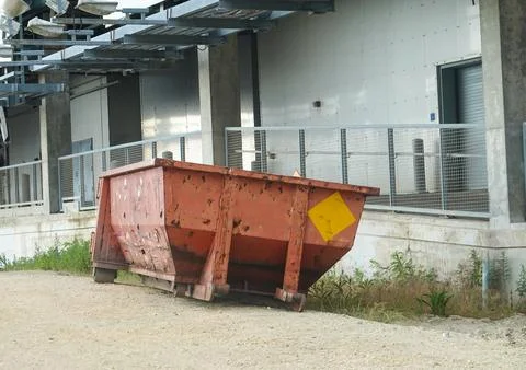Empty rust colored dumpster behind a large building Stock Photos