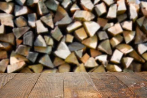 Empty rustic wood table with blurred abstract of stacked up, chopped firewood Stock Photos