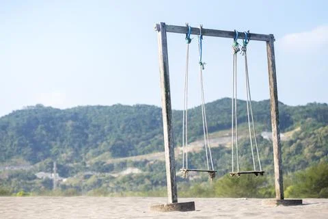An empty rustic wooden swing set stands on a sandy beach dune against a bac.. Stock Photos