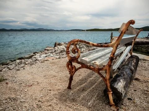 Empty rusty bench on the shore of the sea in calm cloudy day. Stock Photos