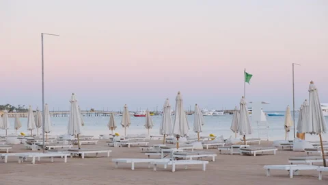 Empty sand beach with сhairs, umbrellas hotel resort town. Sunset, purple sky Stock Footage 196114476