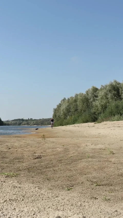 An empty sandy beach with a bald man riding a bicycle along the river. 스톡 동영상 341658892