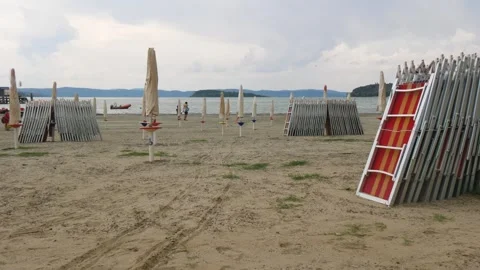 Empty Sandy Beach With Folded Umbrellas and Sunbeds in Cloudy Weather Stock Footage 245428732