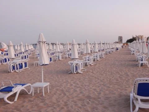 Empty sandy beach with folded umbrellas and sunbeds at sunset Stock Photos
