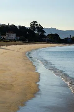 Empty sandy beach with gentle waves at sunrise near coastal town buildings Stock Photos
