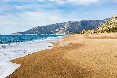 Empty sandy beach with rolling waves and mountain backdrop Stock Photos