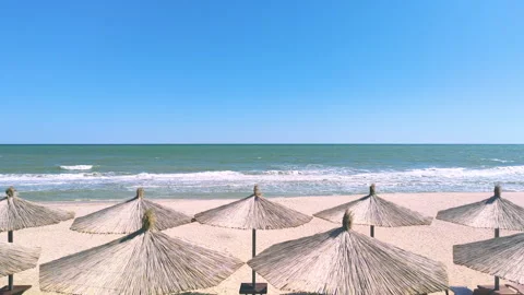 Empty sandy beach. Straw beach umbrellas against the backdrop of sea waves Stock Footage 163460823