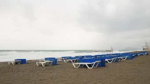 Empty sandy beach with sunbeds at windy stormy day. Dramatic stormy sea with Stock Footage 166599053