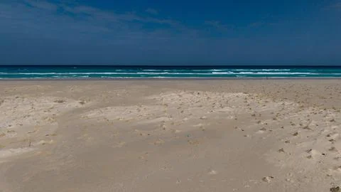 Empty sandy beach with turquoise waves under dark cloudy sky Stock Photos