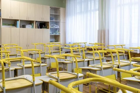 Empty school classroom with yellow desks and chairs arranged in neat rows b.. Stock Photos