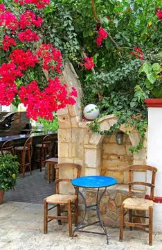 Empty seats and table in taverna under the blooming red flowerd Stock Photos