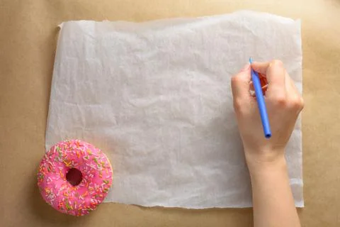 An empty sheet of paper, appetizing pink donut and hand with pen for your tex Stock Photos