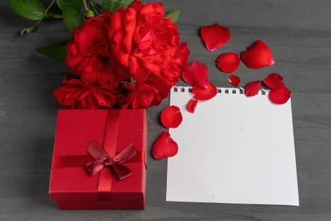 Empty sheet of paper for text and red gift box next to a bouquet and red rose Foto stock