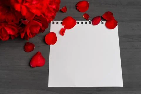 Empty sheet of paper for text next to a bouquet and red rose petals against a Foto stock