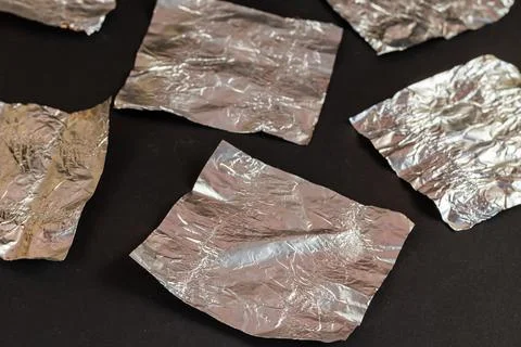 Empty silver candy wrappers on a black background. Crumpled foil from chocola Stock Photos