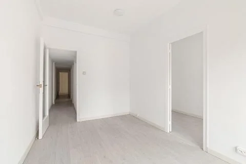 Empty spacious room with light walls and wooden laminate flooring with a Фото