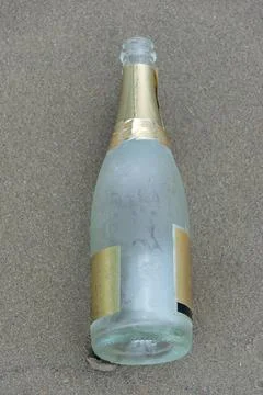 Empty sparkling bottle on the beach sand. Stock Photos
