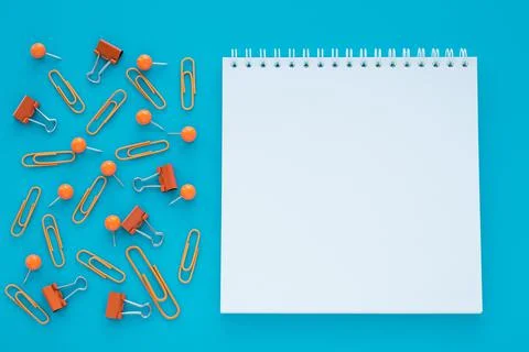 Empty spiral notebook and clips on blue background. Copy space. Education, pl Stock Photos