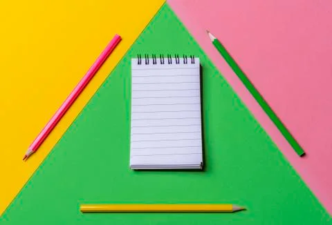 Empty spiral notepad and colorful pencils. Above view. Tricolor background. Stock Photos