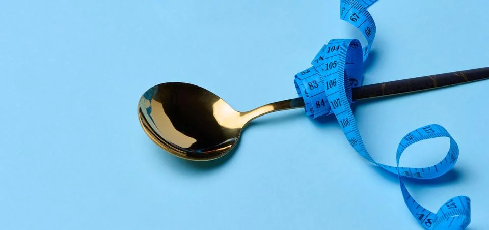 Empty spoon wrapped with centimeter on blue background, weight loss concept Stock Photos