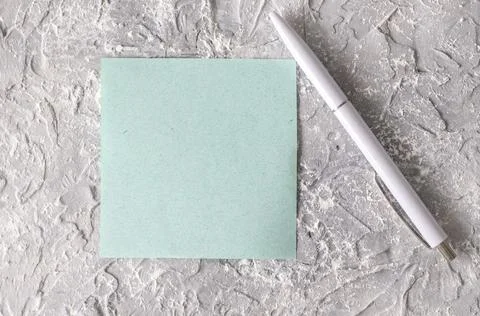 Empty square note blue paper on grey textured concrete next to a white pen. Stock Photos
