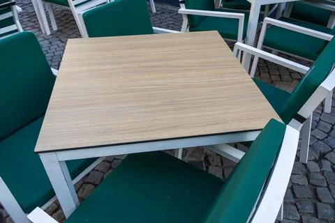 Empty square wooden table with white metal frame surrounded by green cushione Stock Photos