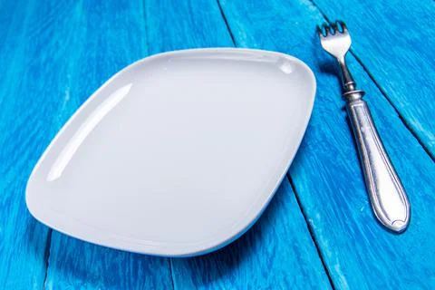 Empty squared white ceramic plate and silver cutlery on blue wooden boards Stock Photos