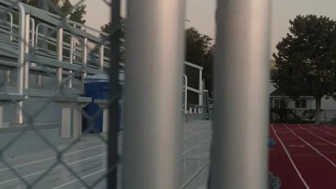Empty stadium bleachers revealed with slow left to right pan past fence posts Video stock 338085631