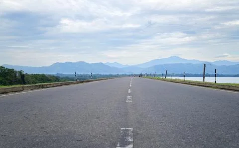 An empty straight road leads to a distant misty mountain range. Scenic land.. Stock Photos