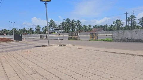 An empty, sun-drenched road and paved area in Kerala, India, bordered by a wall 스톡 동영상 320797023