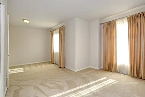 Empty sun filled room features windows dressed in golden curtains hung from l Stock Photos